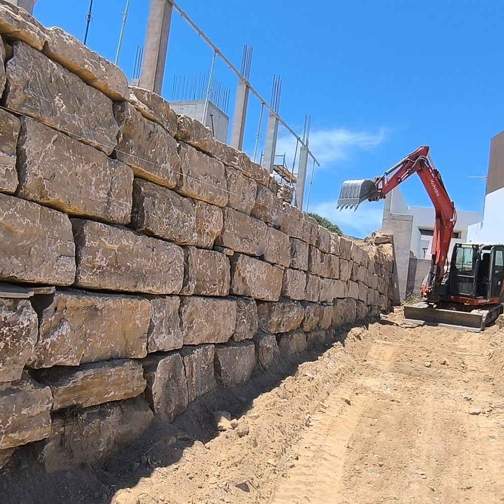 Muro de piedra de tacos en construcción con excavadora en Málaga - MURES Muros de Escollera